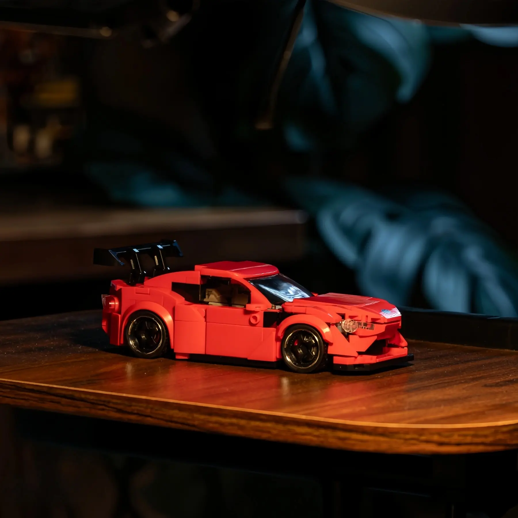 英文: Red Toyota GT86 brick model sports car displayed on a dark wooden table in a modern room setup.